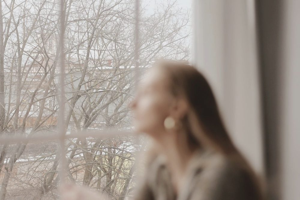 Persona sentada junto a una ventana mirando hacia afuera, con luz cálida
